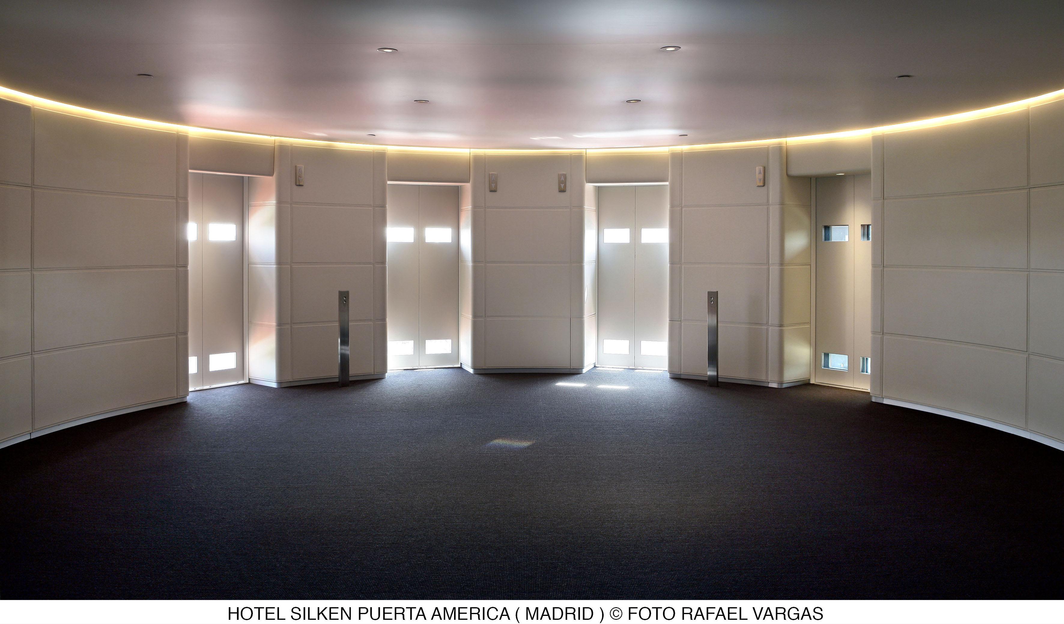 Hotel Puerta America Madrid Esterno foto The photo shows a modern interior space, likely a conference room or lobby, in the Hotel Silken Puerta América in Madrid. The design features a circular layout with multiple doors evenly spaced around the perimeter. The walls have a clean, white fini